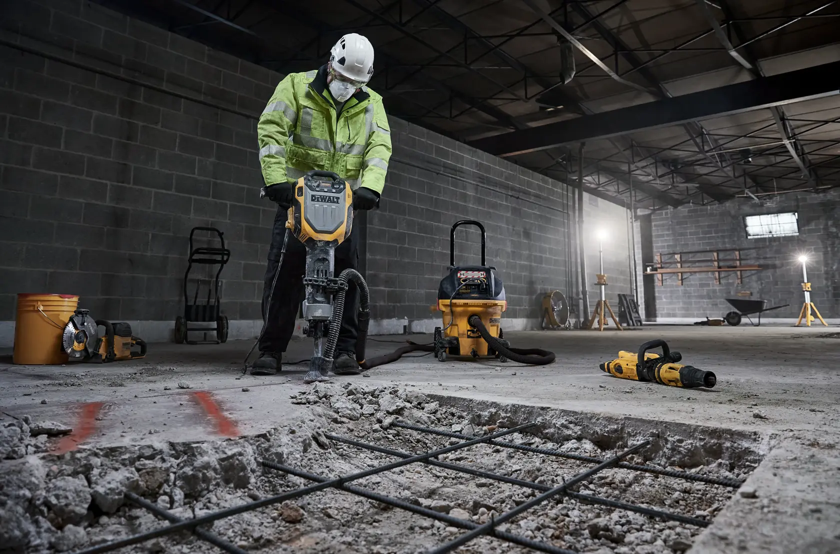 Worker uses DEWALT D25966, D25966-B2 breaker on concrete in warehouse. Construction tools are visible.