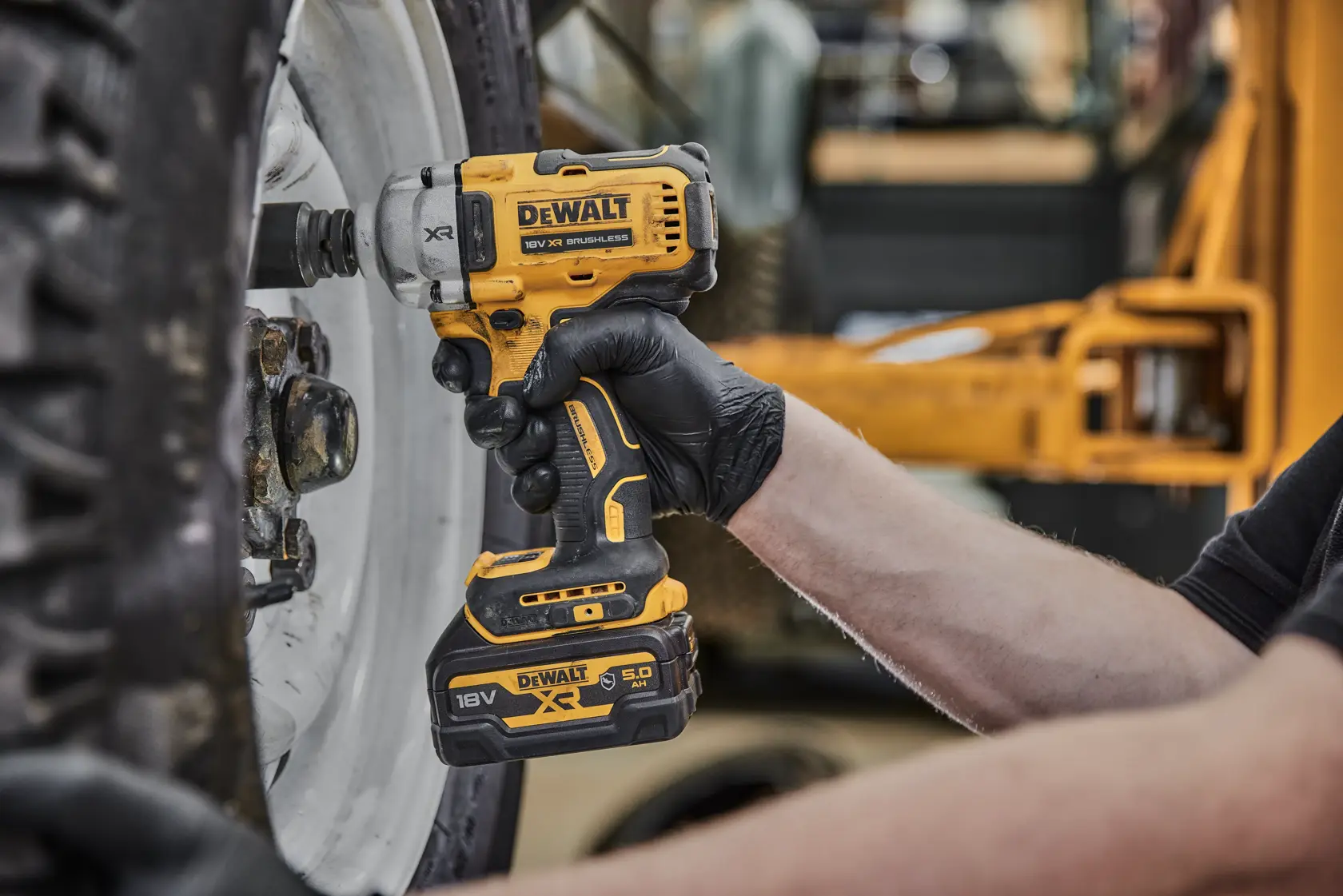 Eine Person mit schwarzen Handschuhen benutzt einen gelben DEWALT Akku-Schlagschrauber (Modell DCF891P2G, 18V XR), um an den Schrauben eines großen Fahrzeugrads zu arbeiten.
