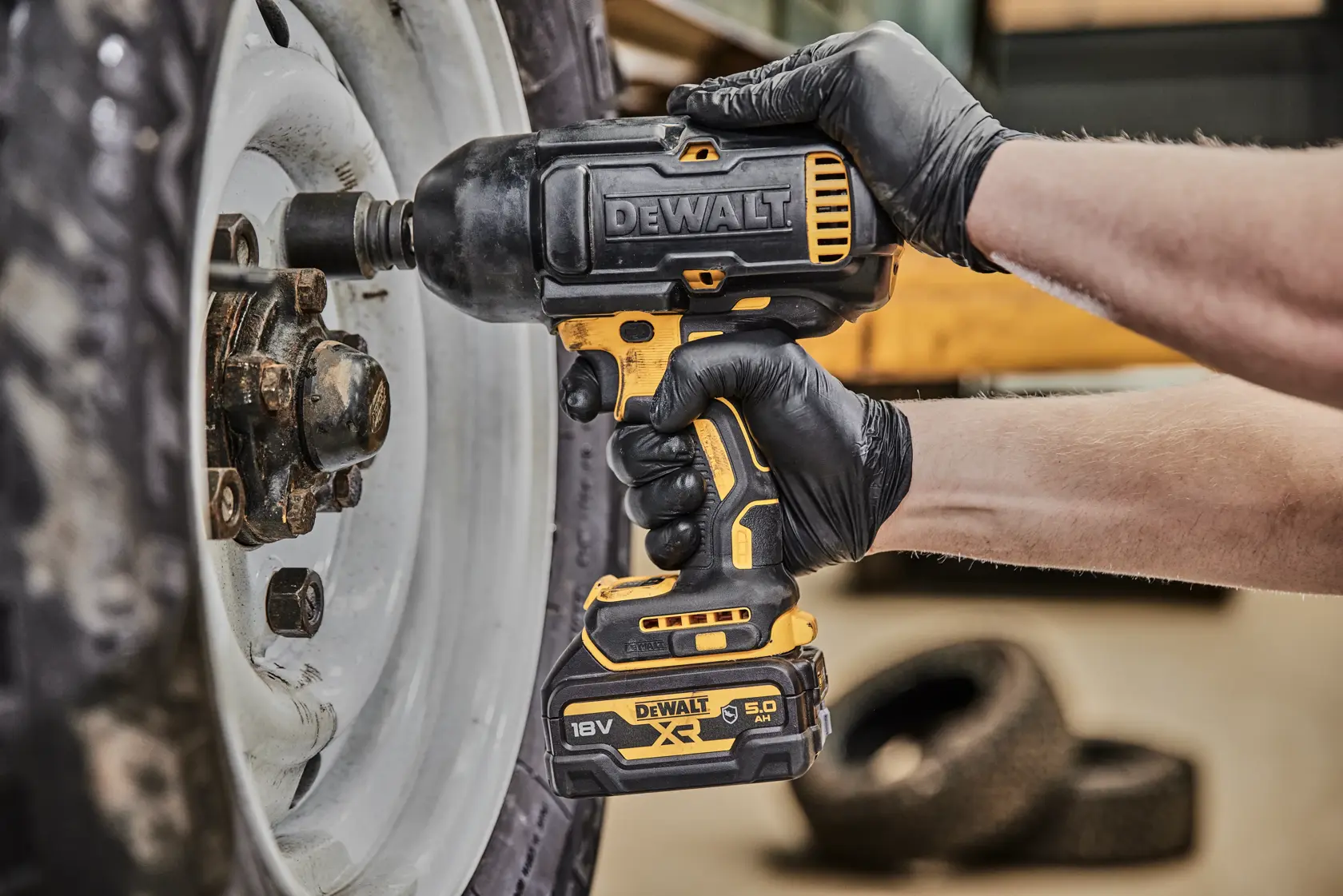DEWALT Akku-Schlagschrauber löst Radmuttern am Fahrzeug, gehalten von einer behandschuhten Hand.
