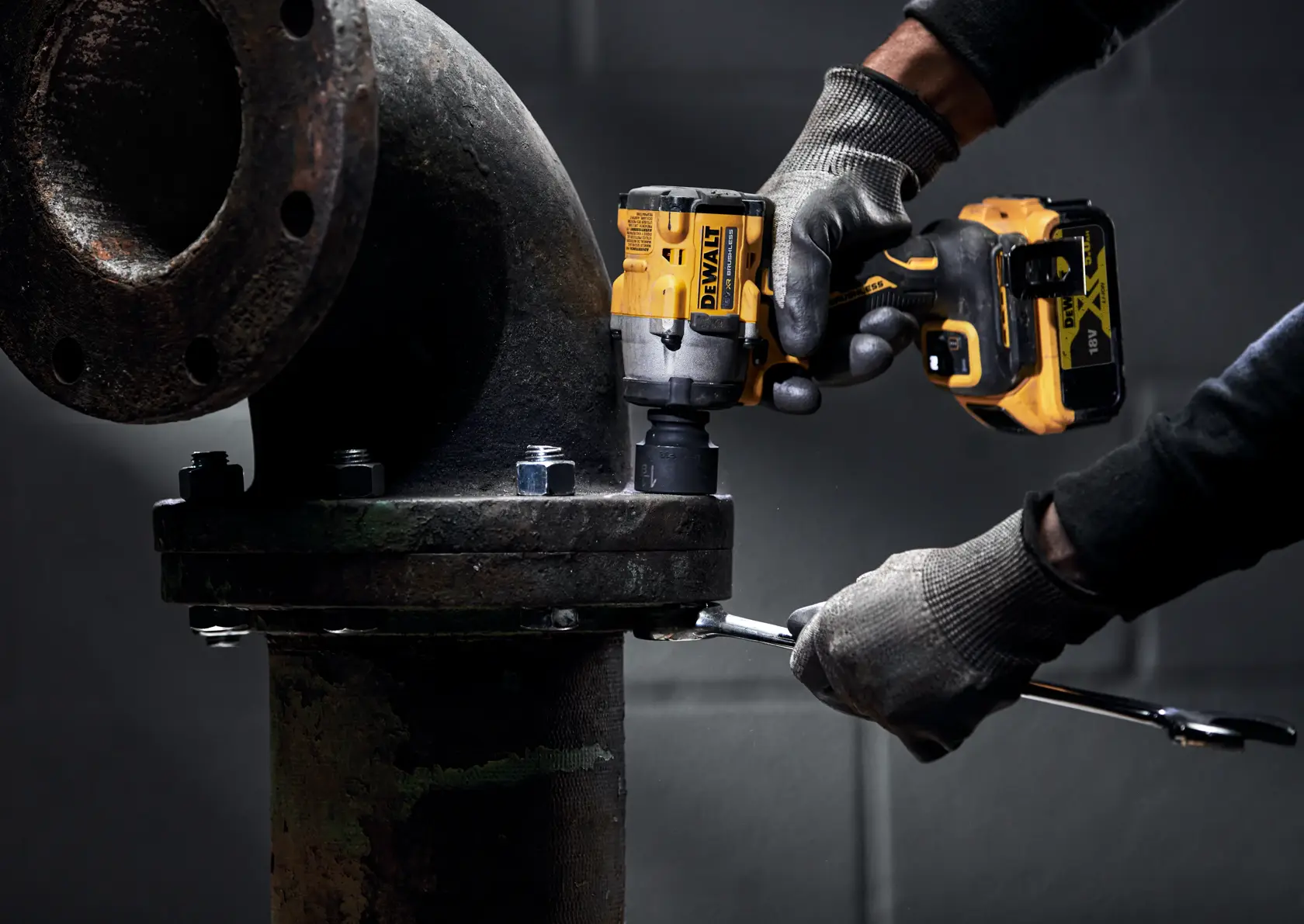 Eine Person mit Handschuhen verwendet einen kabellosen Schlagschrauber von DEWALT, um Schrauben an einem großen Industrie-Rohr festzuziehen.