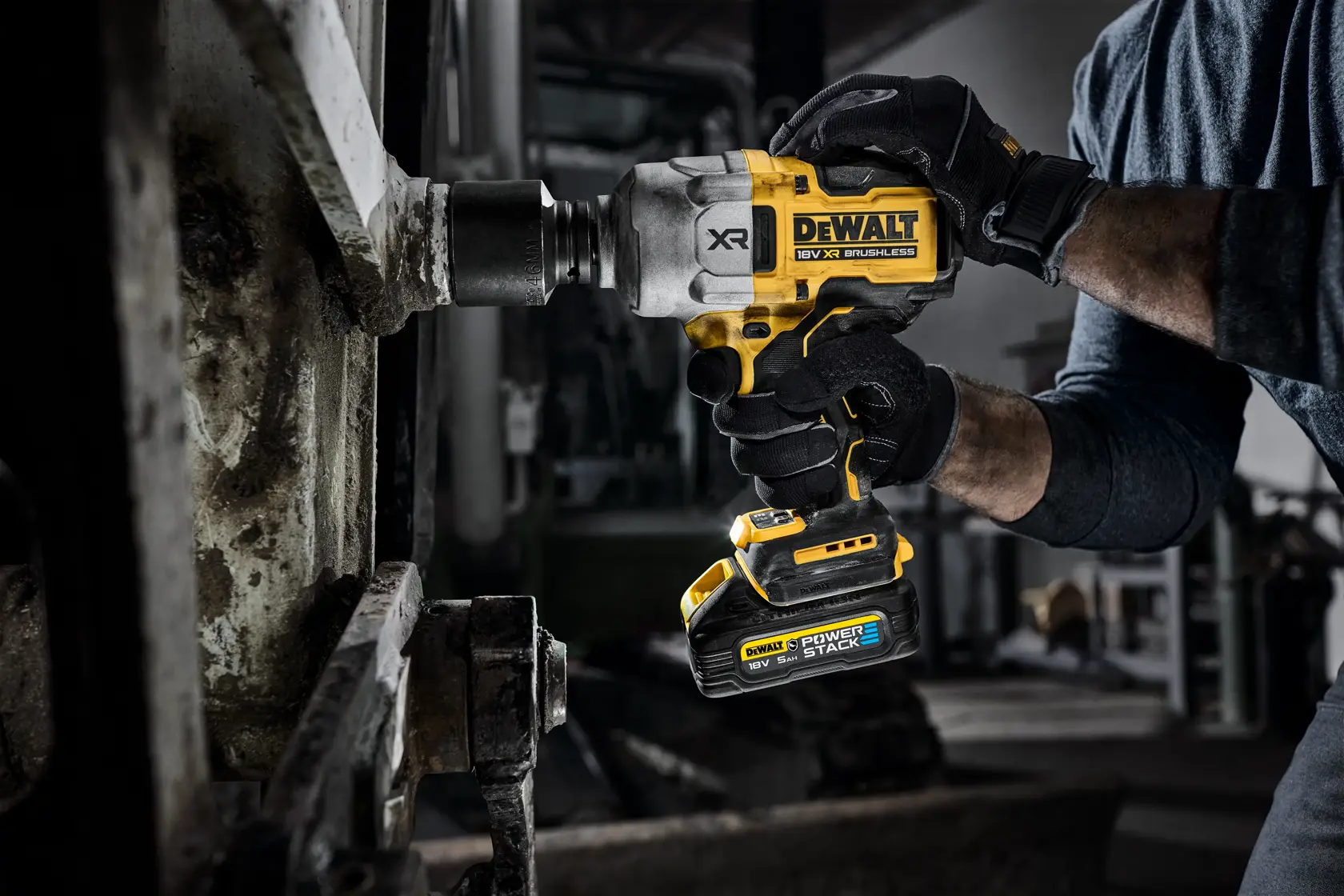 A person uses a DEWALT cordless impact wrench on a metal surface in an industrial setting.