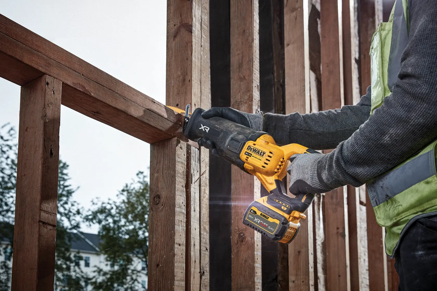 Persona corta una viga de madera con una sierra DEWALT DCS386NT en un sitio de construcción.