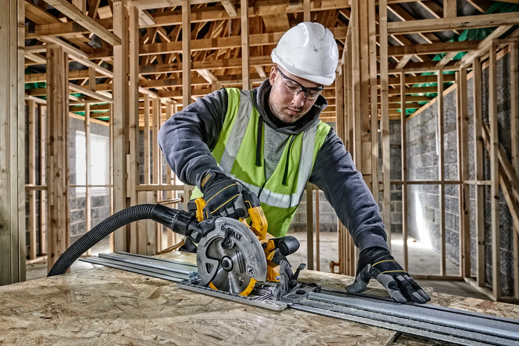 Worker uses DEWALT circular saw to cut wood on construction site, wearing safety gear.