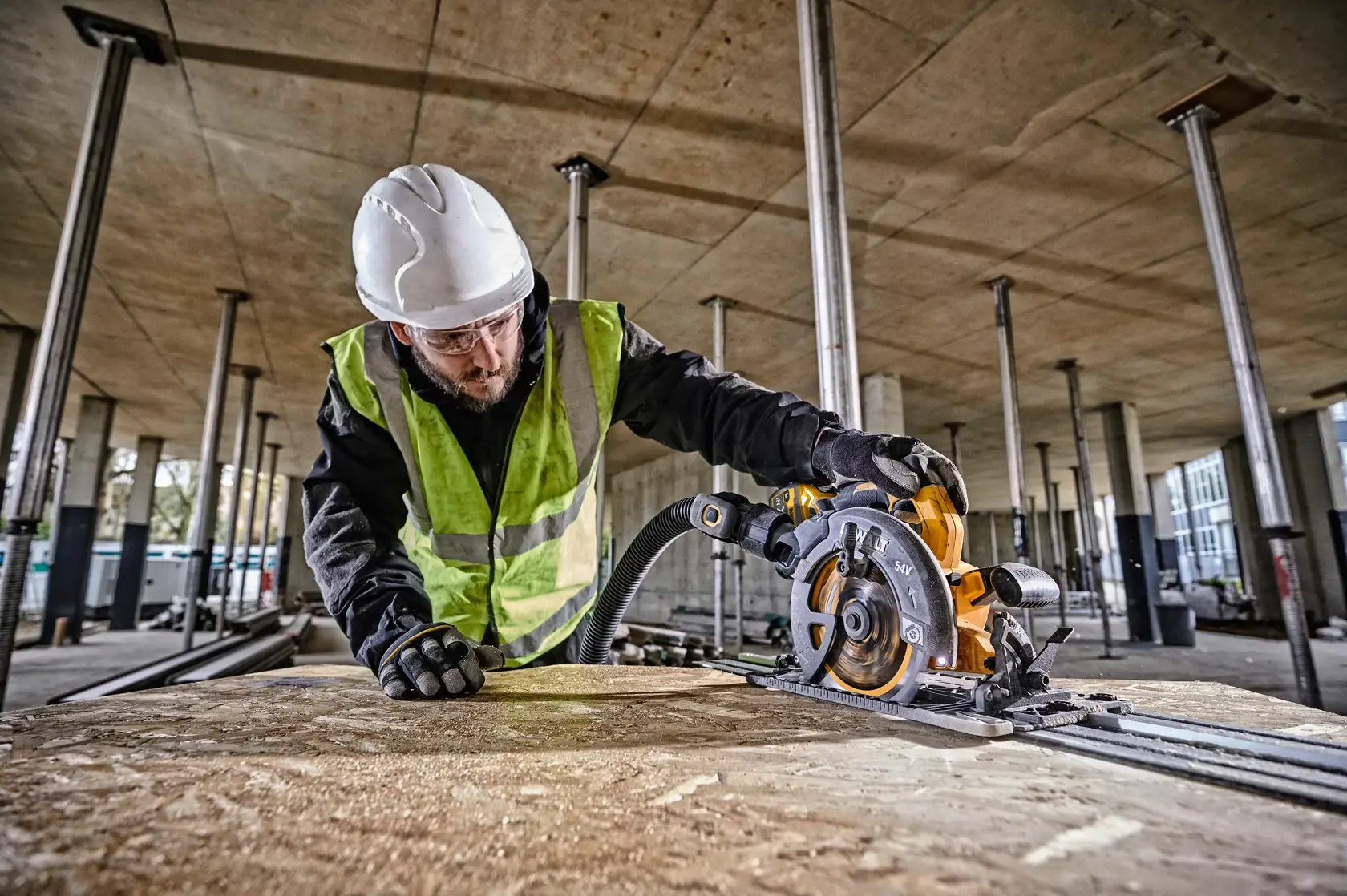 Trabajador corta madera con DEWALT DCS579NT en obra, lleva casco y chaleco reflectante.