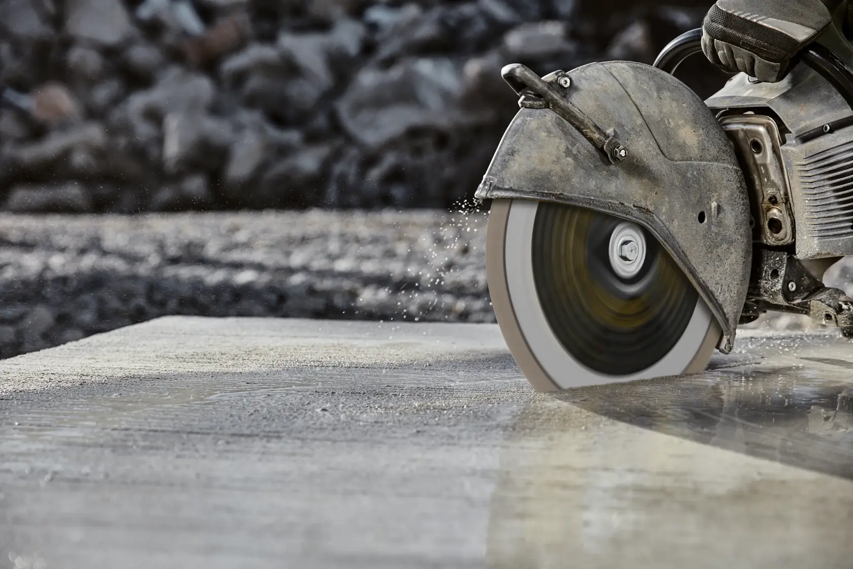 Nahaufnahme einer Motorsäge, die draußen nassen Beton schneidet, Wasser spritzt vom Blatt.