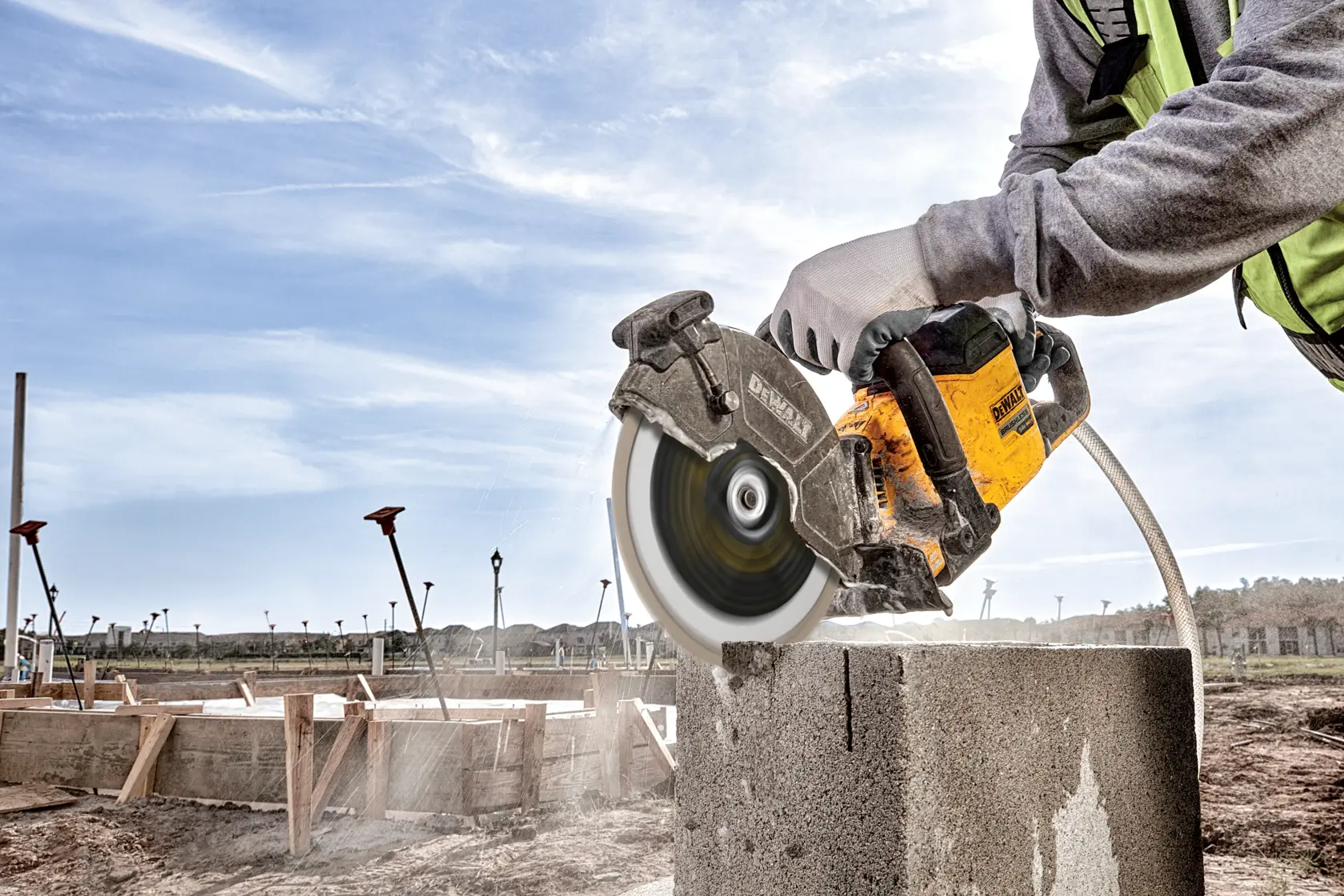 Person schneidet draußen Betonblock mit DEWALT Säge; Staub und Schmutz sichtbar.