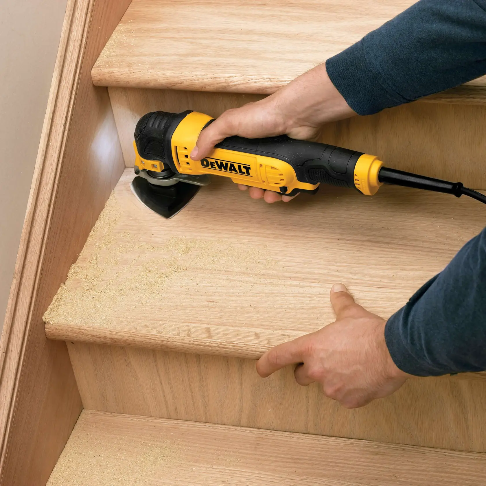Herramienta DEWALT lijando escalón de madera, generando serrín. Manos operando sobre la superficie del escalón.