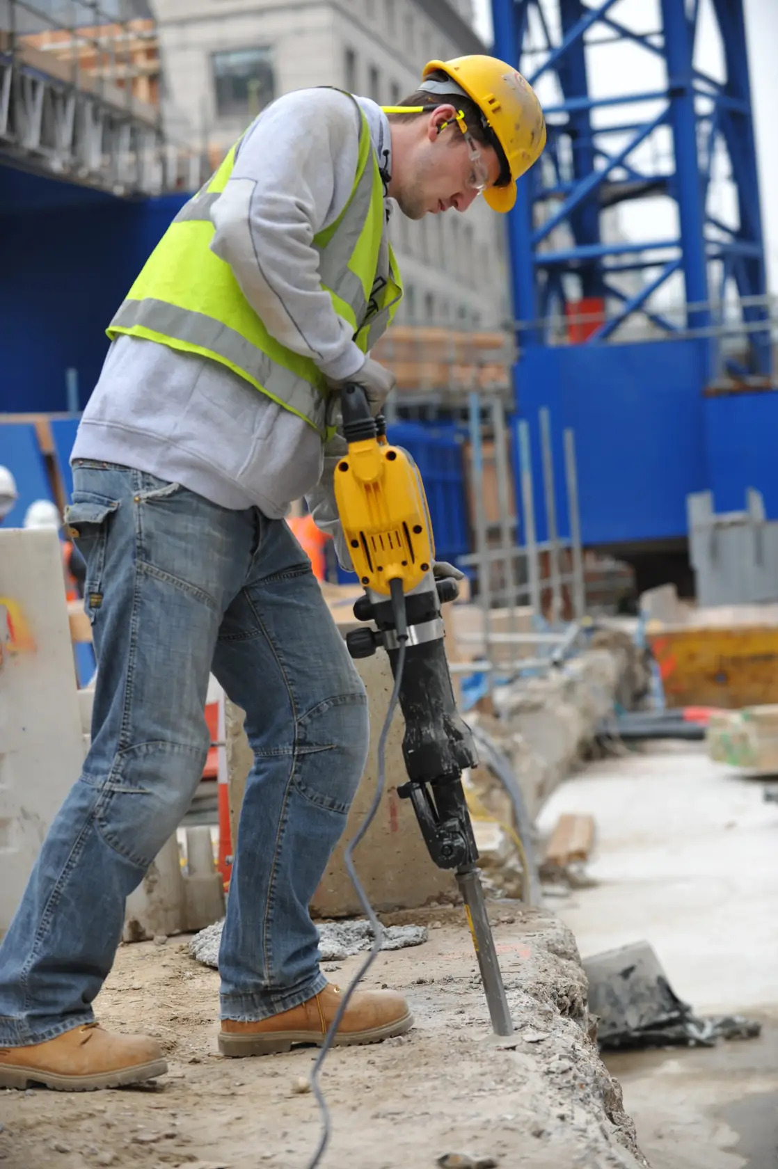 Worker uses a DEWALT DT6929 drill on construction site, wearing safety gear and breaking concrete.