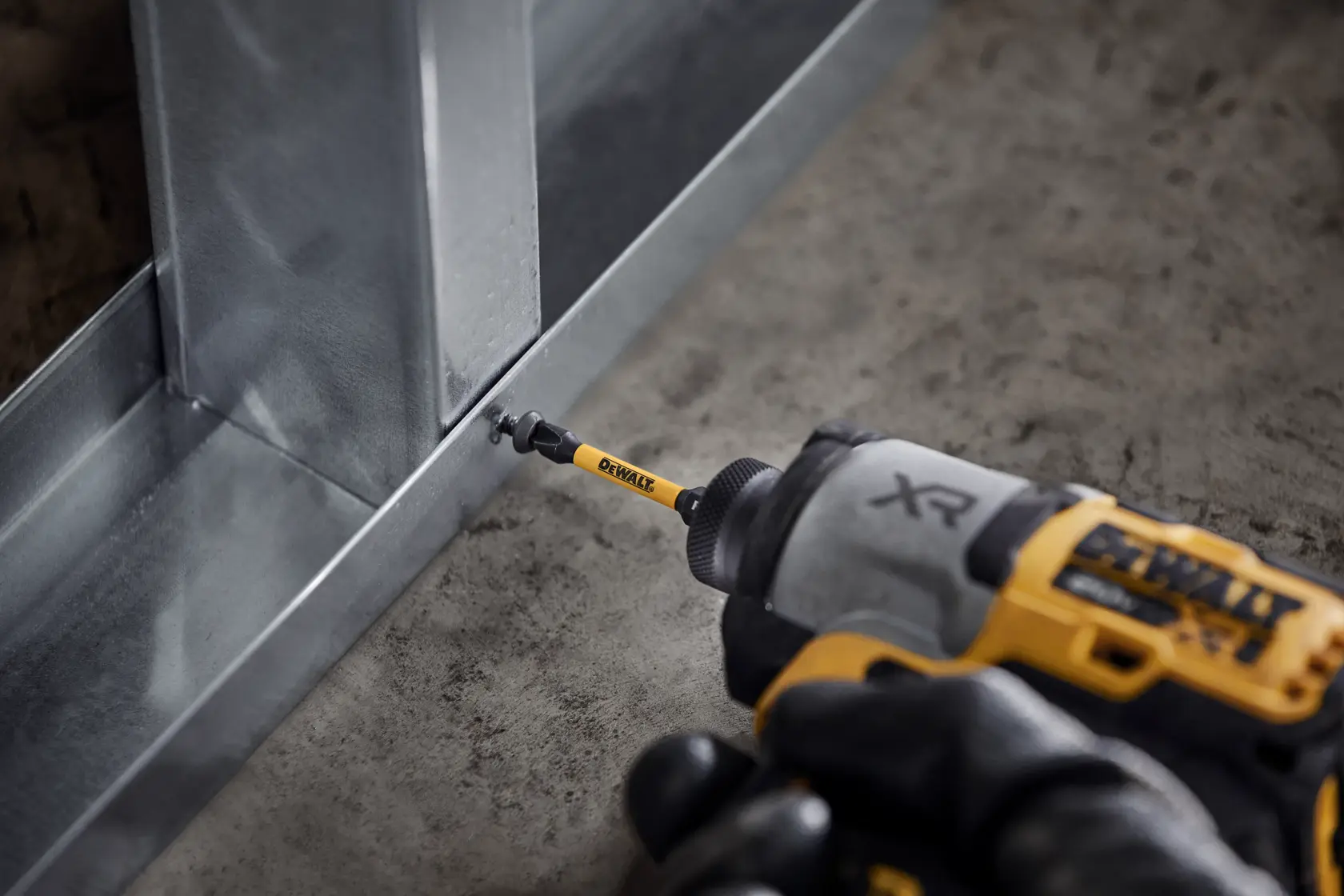 DEWALT drill drives screw into metal frame on concrete floor, close-up of tool and bit in action.