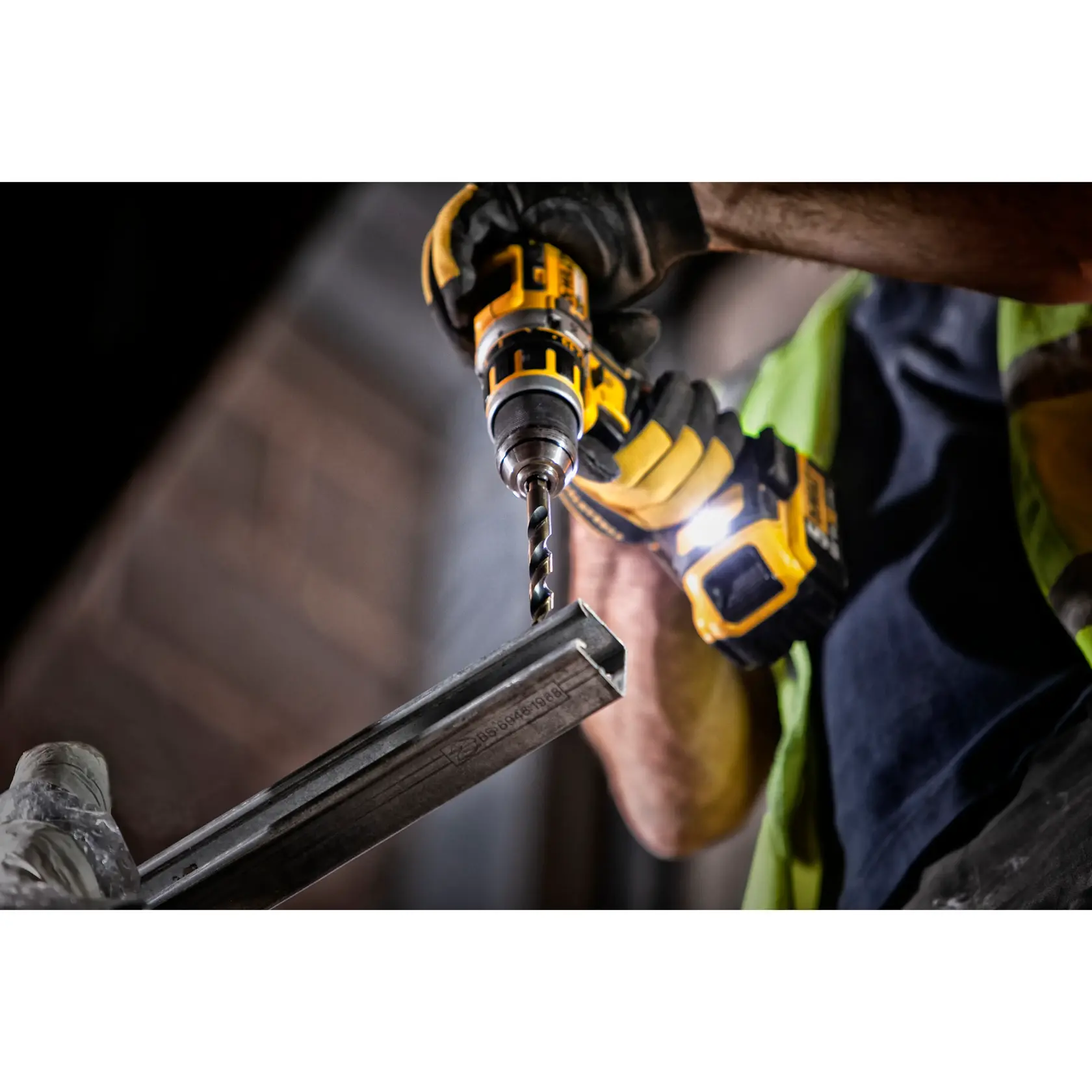 Person bohrt Metall mit gelbem DEWALT Werkzeug und trägt Handschuhe. Nahaufnahme, Industrieumgebung.