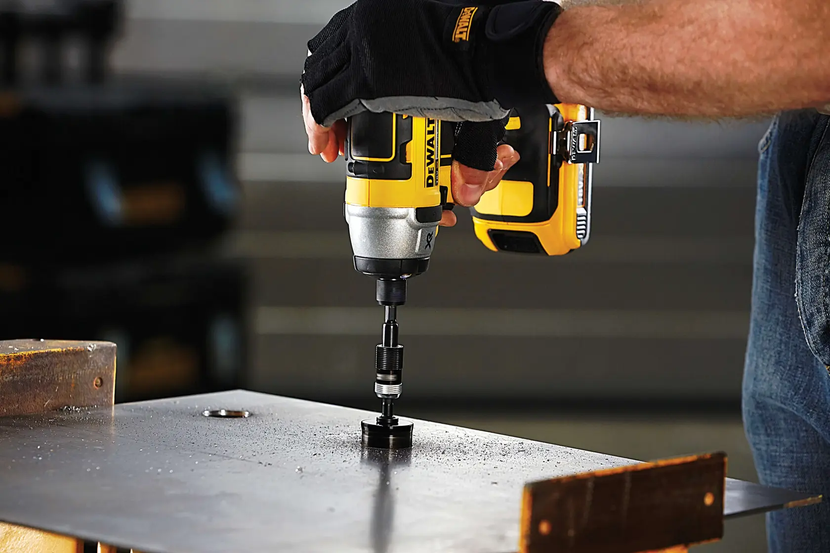 A person uses a DEWALT power drill with attachments to drill through a metal surface. Gloves are worn for safety.