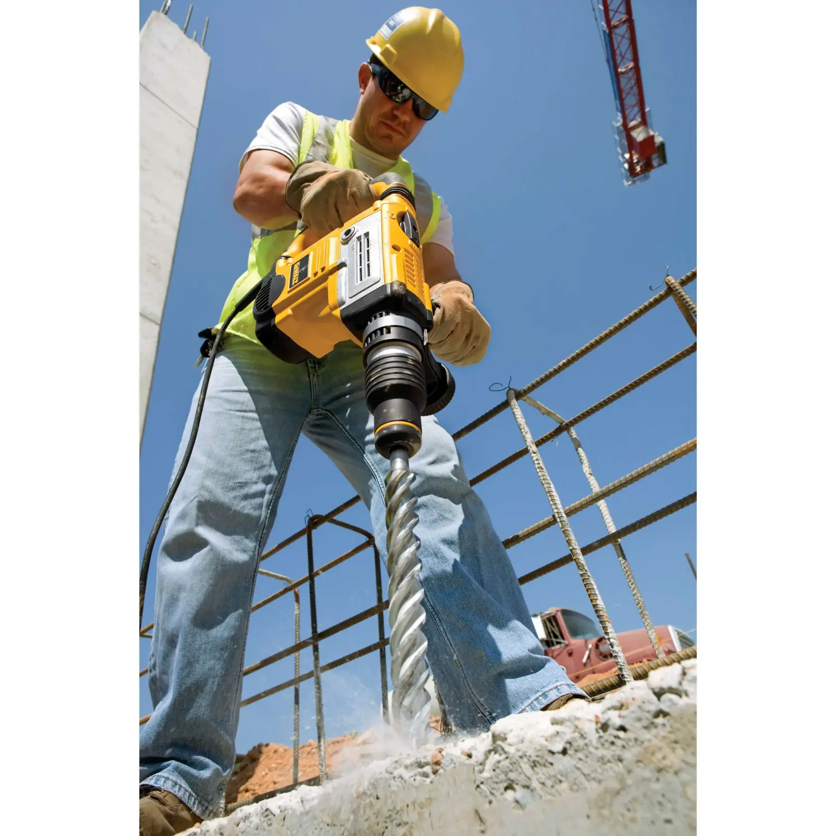 Person bohrt mit einem DEWALT Hammerbohrer DT9418 in Beton auf einer Baustelle unter blauem Himmel.
