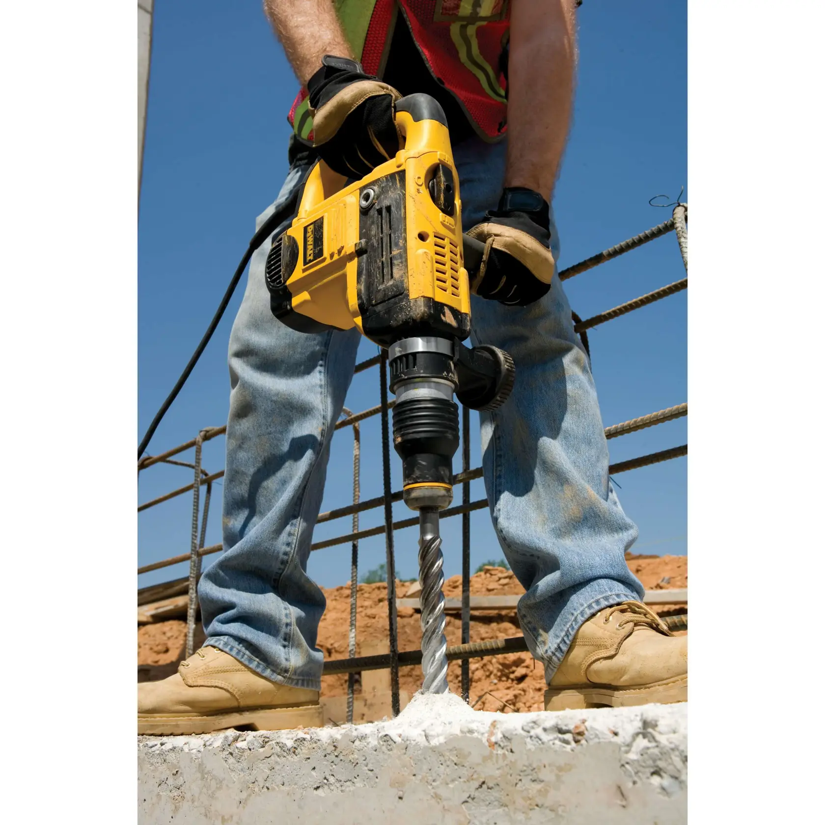 Arbeiter bohrt mit gelbem DEWALT Hammerbohrer in Beton auf einer Baustelle.