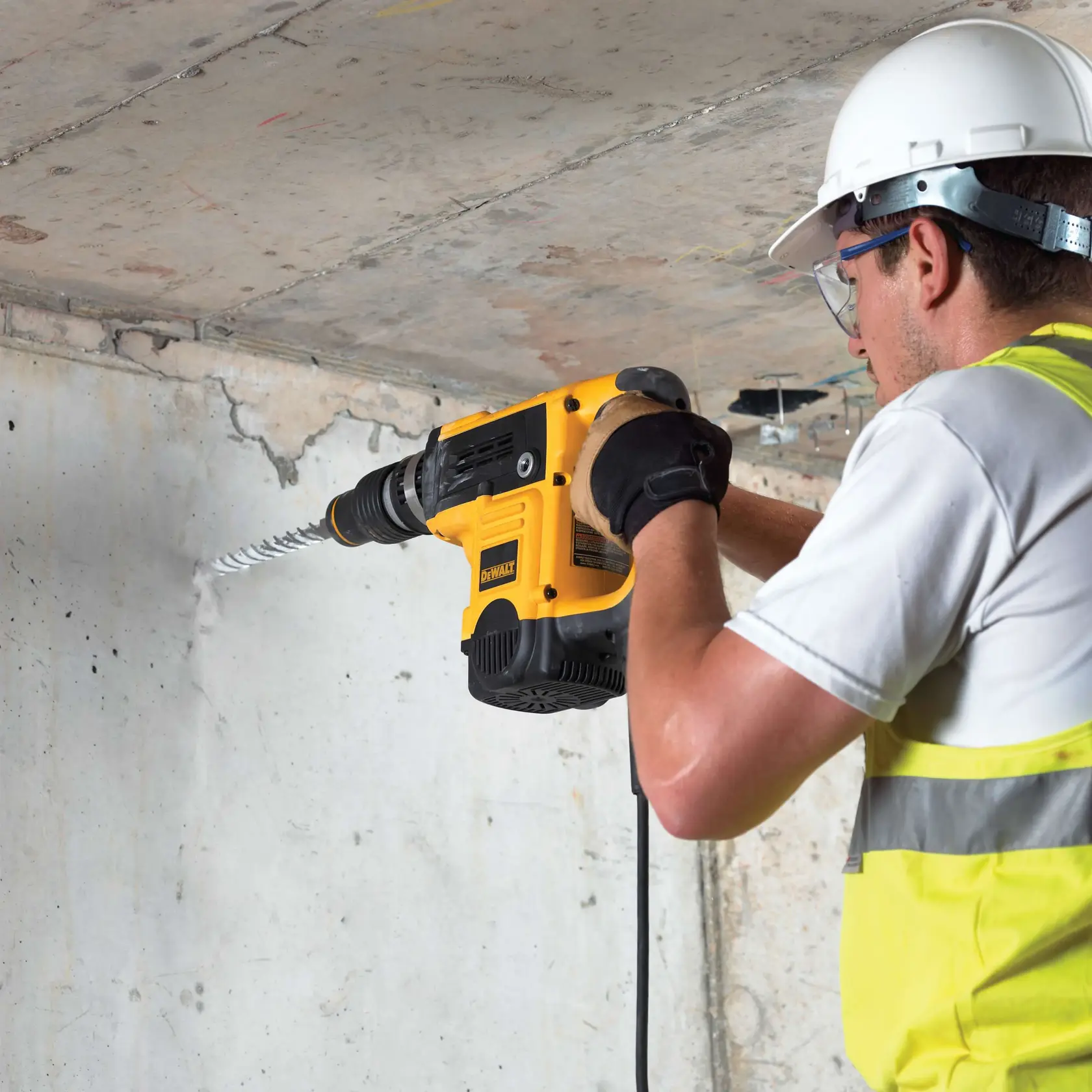 Arbeiter nutzt DEWALT Bohrhammer an Betonwand. Trägt Schutzkleidung und Warnweste.