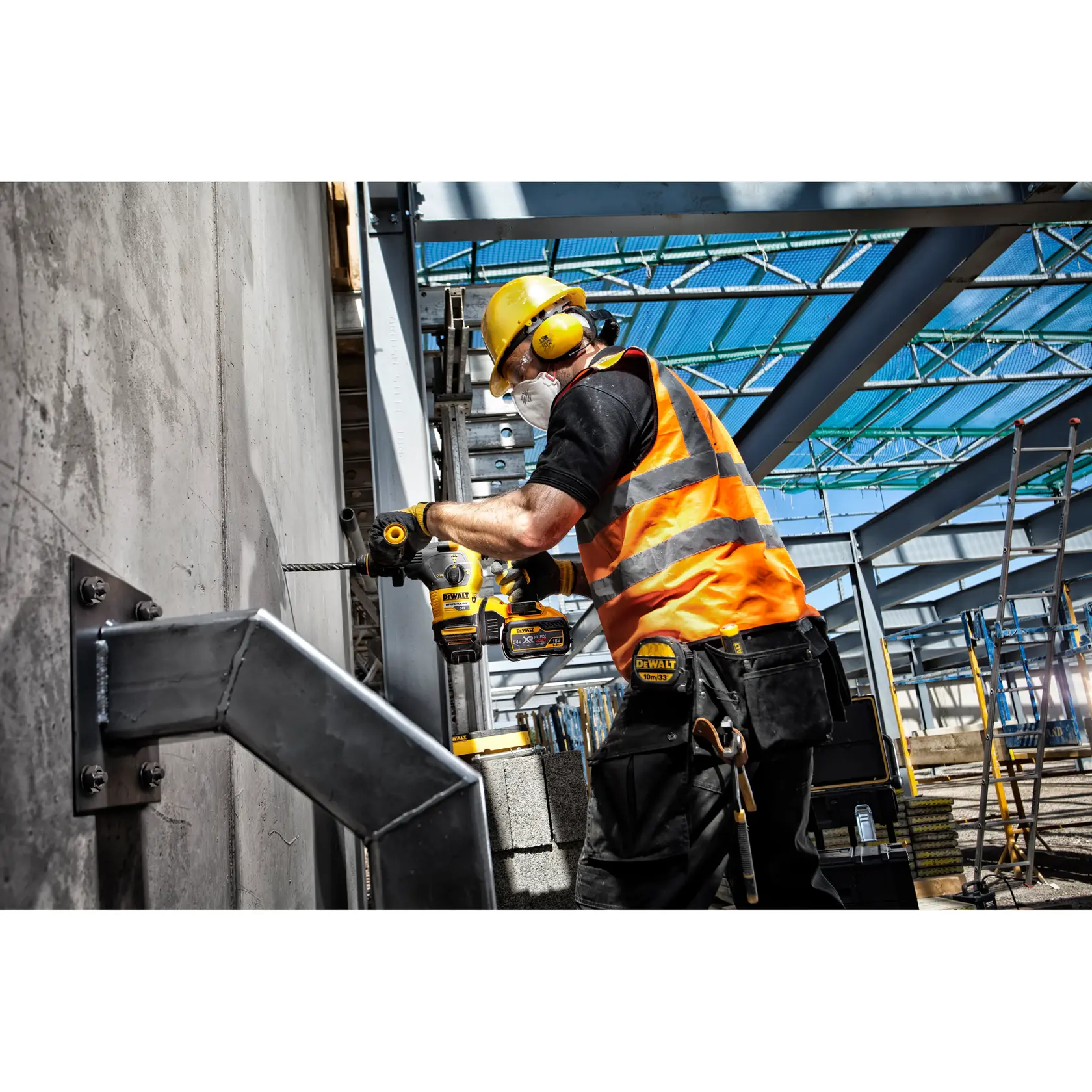 Worker in safety gear uses DEWALT drill on concrete wall at a construction site with steel beams.