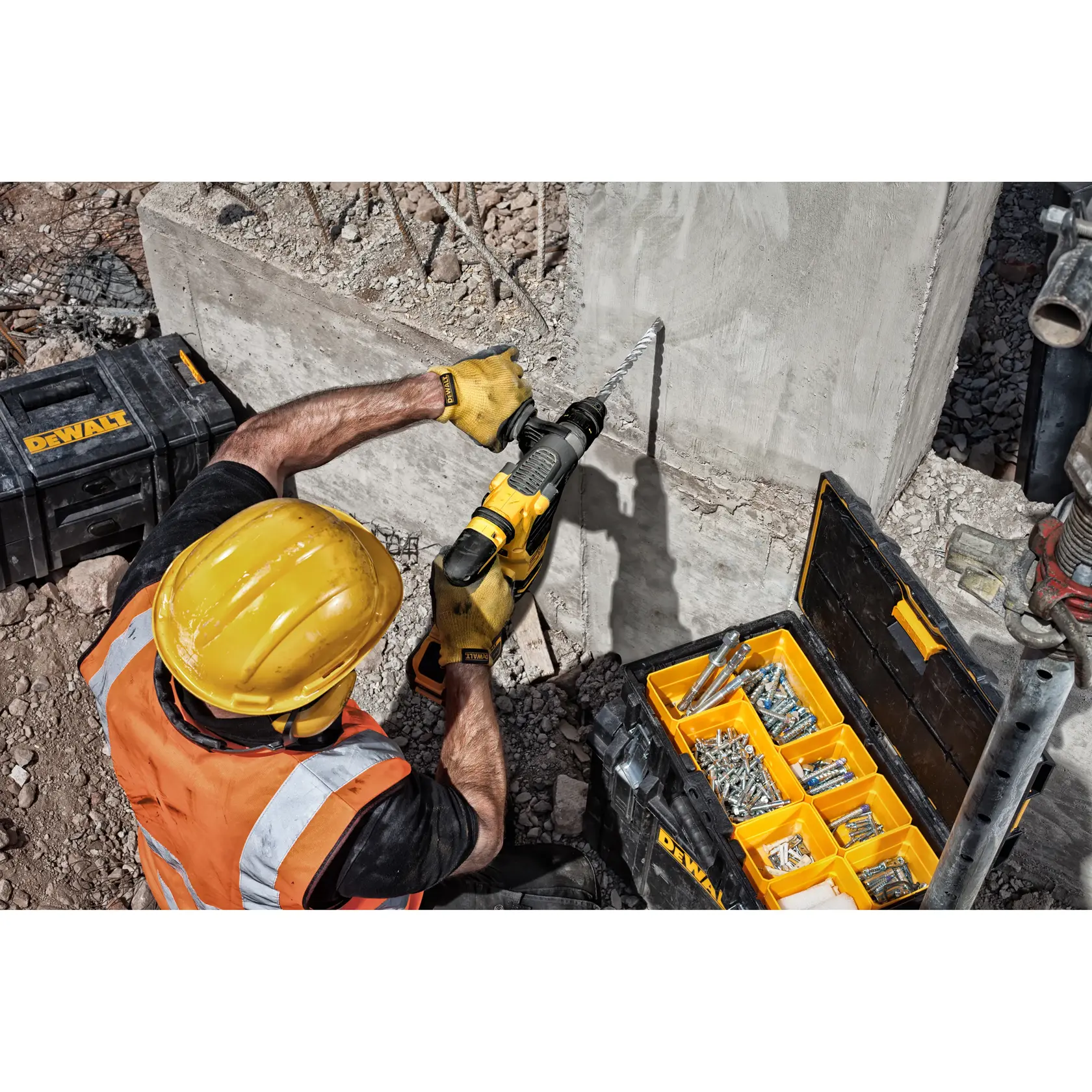 Trabajador perfora pared de concreto con herramienta DEWALT, caja abierta con fijaciones metálicas, obra.