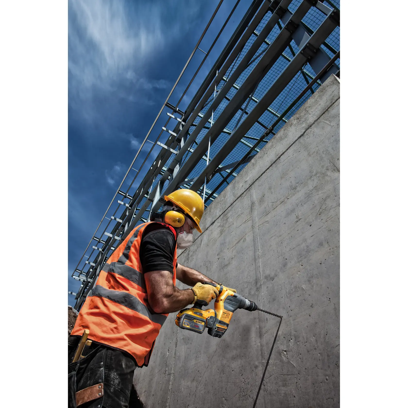 Trabajador perfora pared de cemento con herramienta DEWALT, lleva chaleco naranja y equipo de seguridad.