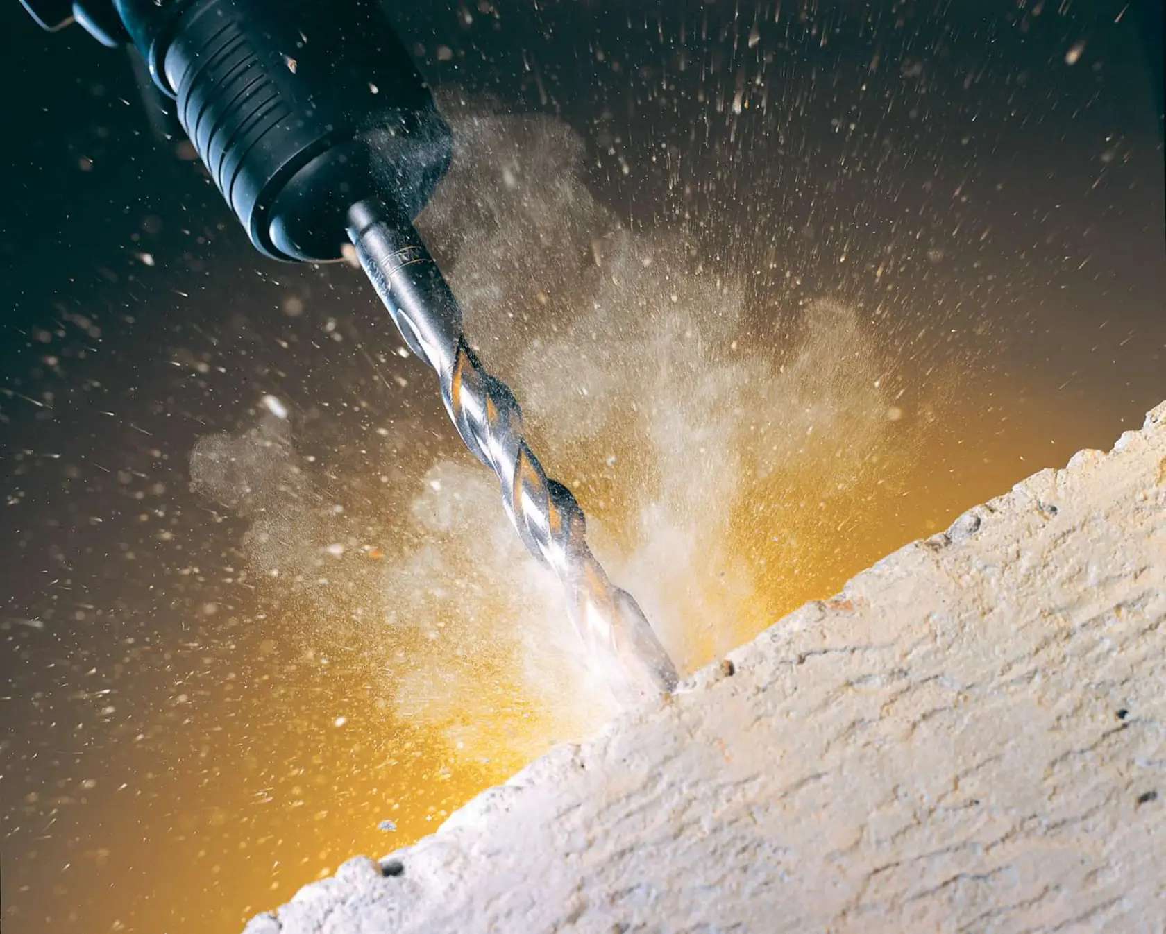 Close-up of a DEWALT drill bit creating dust while drilling into concrete.